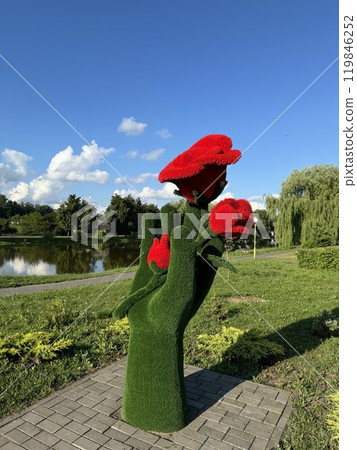 Artistic Green Hand Sculpture Holding Bright Red Flowers in a Scenic Park 119846252