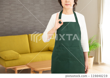 一位身穿綠色圍裙的高級女家庭主婦/管家在她家的客廳裡做一個圓圈標誌 119848219