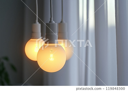 Trio of soft glowing light bulbs with a minimalist design, hanging in front of a sheer white curtain 119848300