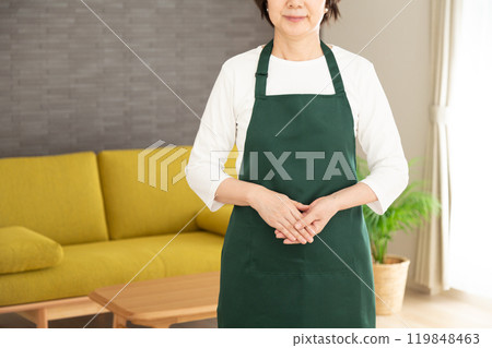 一位身穿綠色圍裙的高級女家庭主婦/管家在她家的客廳裡微笑 119848463