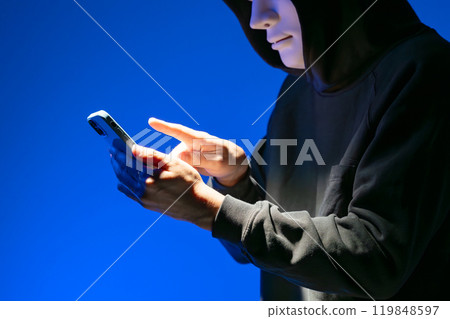 Masked hacker operating a smartphone Masked hacker operating a smartphone 119848597