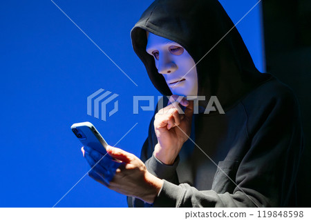 Masked hacker operating a smartphone 119848598