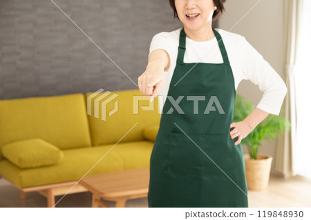 A senior woman housewife/housekeeper wearing a green apron who found something in the living room at home 119848930