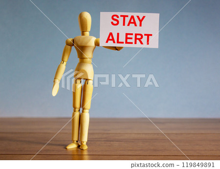 Wooden model of a man holding a tablet saying 'stay alert'. COVID-19 pandemic concept. Wooden model of a man holding a tablet saying 'stay alert'. COVID-19 pandemic concept. 119849891