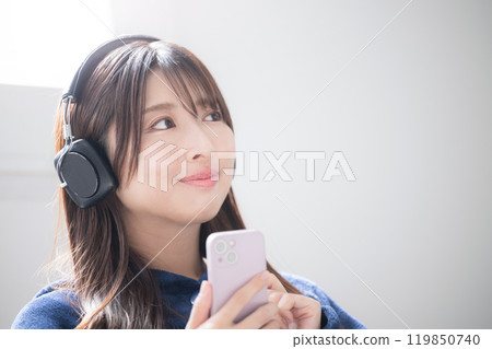 Close-up image of a singing young woman listening to music wearing headphones and looking up, copy space available 119850740