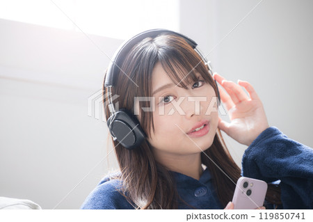 Close-up looking-at-camera image of a young woman wearing headphones and singing listening to music, copy space available 119850741