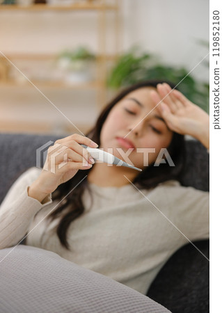 A woman is holding a thermometer and looking at it A woman is holding a thermometer and looking at it 119852180