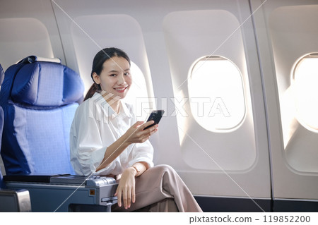 A woman is sitting on a plane with a cell phone in her hand 119852200
