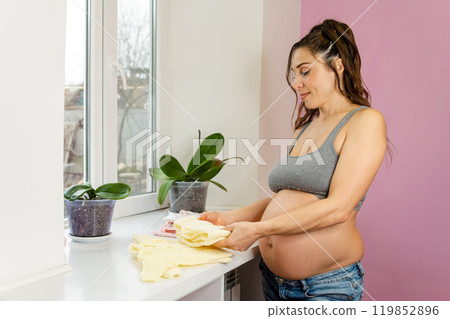 Mother lovingly prepares for her new arrival, sorting through soft baby clothes 119852896