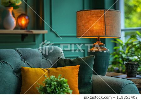 Warm evening in cozy living room interior. A couch is covered with blue and orange pillows, ceramic lamp and cold season decorations. Concept of home decor, comfort, and relaxation. 119853402