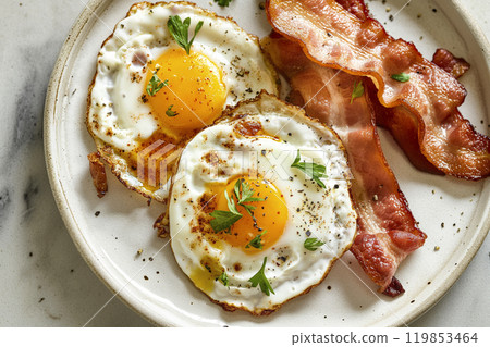 Eggs and bacon, top view on fresh made breakfast on a table ready to eat. Fried eggs, crispy bacon slices, traditional minimalist breakfast Eggs and bacon, top view on fresh made breakfast on a table ready to eat. Fried eggs, crispy bacon slices, traditional minimalist breakfast 119853464