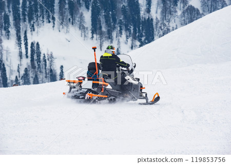 Rescuer man driving snowmobile on the ski resort. Rescuer man driving snowmobile on the ski resort. 119853756