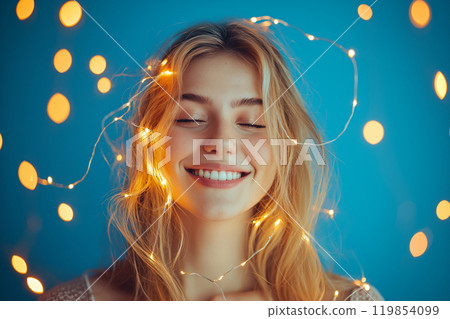 Happy young woman with glowing light strings around her head, a concept of mindfulness, meditation, creativity inspiration. Cozy home Christmas time, decorative Christmas twinkling string lights 119854099