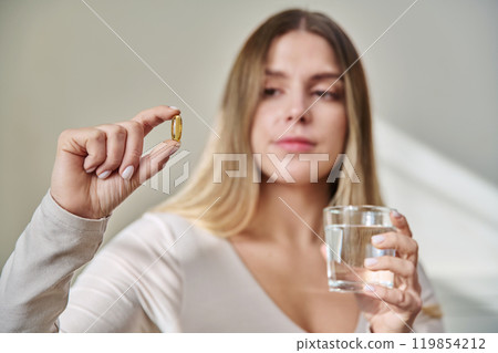 Close up of yellow omega 3 fish oil capsule in hand of young woman. Close up of yellow omega 3 fish oil capsule in hand of young woman. 119854212