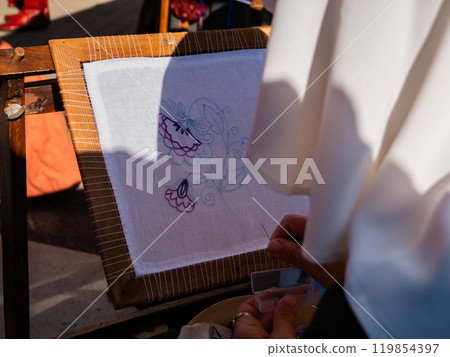 close-up shot of a woman from behind embroidering a flower on a white framed canvas close-up shot of a woman from behind embroidering a flower on a white framed canvas 119854397