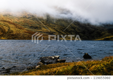 A serene lake reflects the surrounding misty hills during late autumn, creating a peaceful atmosphere in a natural landscape rich with earthy colors and texture. A serene lake reflects the surrounding misty hills during late autumn, creating a peaceful atmosphere in a natural landscape rich with earthy colors and texture. 119855060