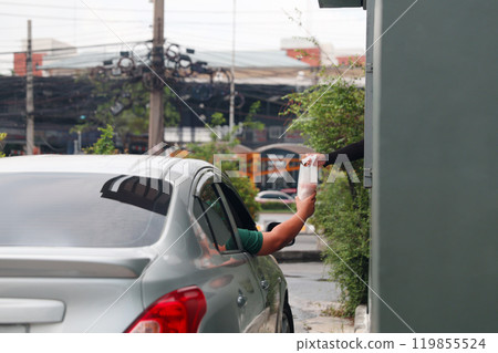 Hand Man in car receiving coffee in drive thru fast food restaurant. Staff serving takeaway order for driver in delivery window. Drive through and takeaway for buy fast food for protect covid19. Hand Man in car receiving coffee in drive thru fast food restaurant. Staff serving takeaway order for driver in delivery window. Drive through and takeaway for buy fast food for protect covid19. 119855524