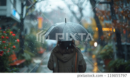 A woman is walking down a street in the rain with an umbrella 119855797