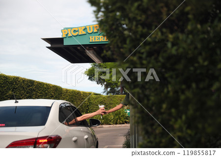 Hand Man in car receiving coffee in drive thru fast food restaurant. Staff serving takeaway order for driver in delivery window. Drive through and takeaway for buy fast food for protect covid19. 119855817