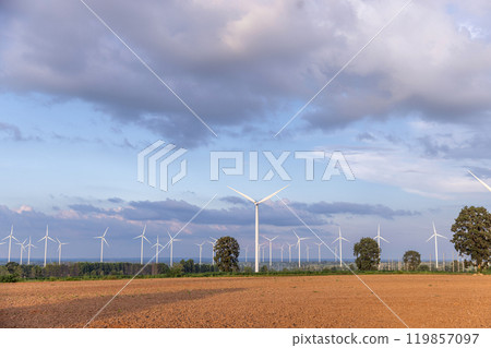 View of wind farm or wind park, with high wind turbines for generation electricity. A wind farm is a group of turbines that are located in a single area and are connected to a power grid View of wind farm or wind park, with high wind turbines for generation electricity. A wind farm is a group of turbines that are located in a single area and are connected to a power grid 119857097
