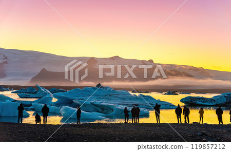 Ice Lagoon. Silhouette of tourists taking photo of sunset Ice lagoon. South Iceland, Jokulsarlon Ice Waterfall. Great tourist attraction. Ice Lagoon. Silhouette of tourists taking photo of sunset Ice lagoon. South Iceland, Jokulsarlon Ice Waterfall. Great tourist attraction. 119857212
