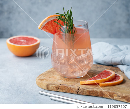 Homemade grapefruit lemonade with rosemary and ice in a glass on a wooden board on a blue background 119857507