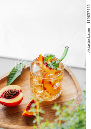 Peach lemonade with ice and mint on a wooden board on a white table. Fresh iced tea in a glass Peach lemonade with ice and mint on a wooden board on a white table. Fresh iced tea in a glass 119857533