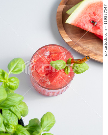 Glass of refreshing watermelon cocktail with basil and ice on a light background with fresh herb  119857547