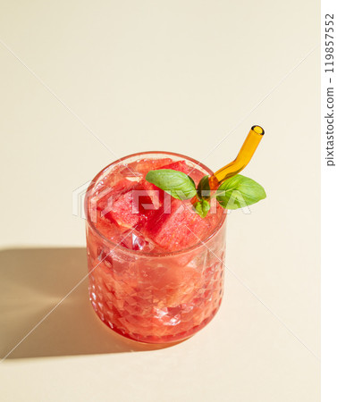 Glass of refreshing watermelon cocktail with basil and ice on a yellow background with shadow. Glass of refreshing watermelon cocktail with basil and ice on a yellow background with shadow. 119857552