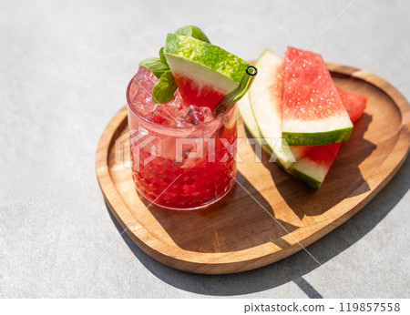 Glass of refreshing watermelon cocktail with basil, ice on wooden board with fruit slices Glass of refreshing watermelon cocktail with basil, ice on wooden board with fruit slices 119857558