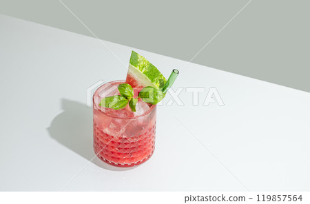 Glass of refreshing watermelon smoothie with basil, ice on white and green background with shadow. Glass of refreshing watermelon smoothie with basil, ice on white and green background with shadow. 119857564