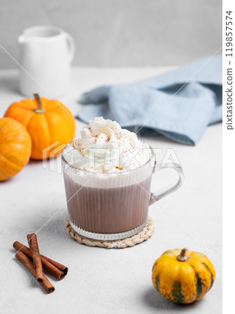 Hot chocolate with whipped cream in glass cup on light background with decorative pumpkins Hot chocolate with whipped cream in glass cup on light background with decorative pumpkins 119857574