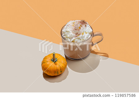 Spice latte with whipped cream in glass cup on orange background with decorative pumpkin and shadow. Spice latte with whipped cream in glass cup on orange background with decorative pumpkin and shadow. 119857586