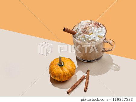 Spice pumpkin latte in glass cup on orange background with decorative pumpkins, cinnamon sticks Spice pumpkin latte in glass cup on orange background with decorative pumpkins, cinnamon sticks 119857588