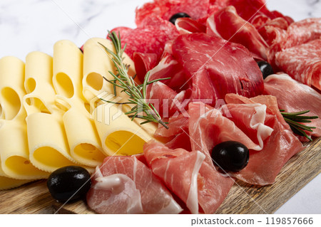 Assorted meat, appetizer, prosciutto, salami and ham, with maasdam cheese and olives, on a wooden board, breakfast, top view, close-up, no people Assorted meat, appetizer, prosciutto, salami and ham, with maasdam cheese and olives, on a wooden board, breakfast, top view, close-up, no people 119857666