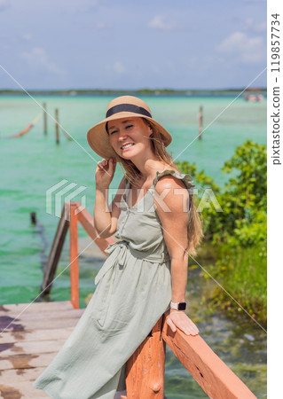 Female tourist in a turquoise dress standing on a wooden pier over the turquoise waters of Bacalar Lake, Mexico. Peaceful tropical travel destination concept 119857734
