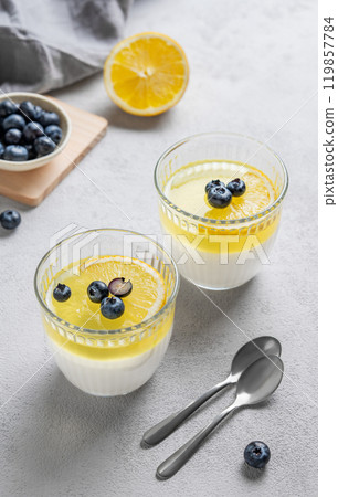 lemon panna cotta with blueberries in two glasses on a light background with berries  and spoons. 119857784