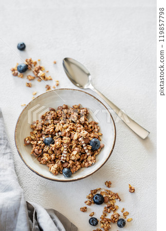 Granola with blueberries in a bowl on a light background with fresh berries, spoon Granola with blueberries in a bowl on a light background with fresh berries, spoon 119857798