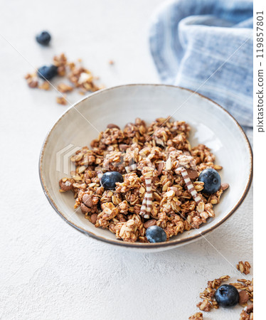 Dry granola with blueberries in a bowl on a light background with fresh berries, napkin 119857801