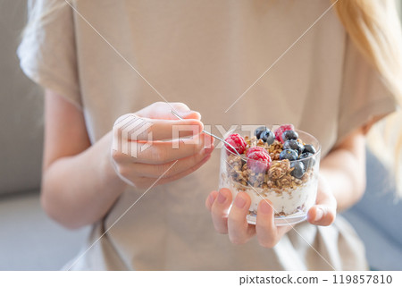 Granola with greek yogurt, raspberries and blueberries in a glass in hands of a woman Granola with greek yogurt, raspberries and blueberries in a glass in hands of a woman 119857810