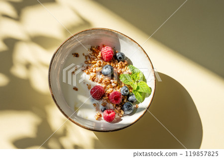 Granola with greek yogurt, raspberries and blueberries in a bowl on a yellow background Granola with greek yogurt, raspberries and blueberries in a bowl on a yellow background 119857825
