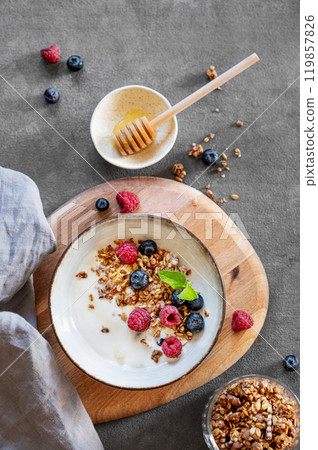 Granola with greek yogurt, raspberries, blueberries and honey in a bowl on a wooden board  119857826