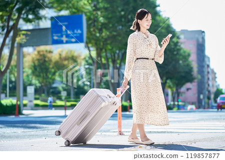 帶著手提箱和智慧型手機在城裡行走的年輕女子 119857877