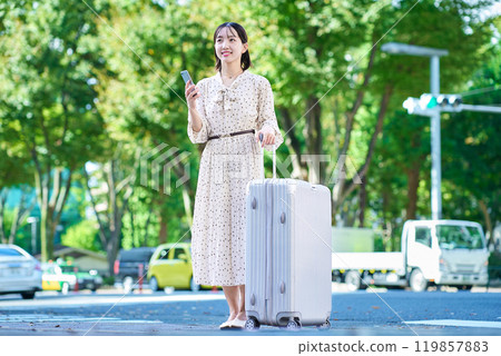 Young woman walking through the city with a suitcase and a smartphone 119857883