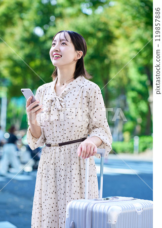 Young woman walking through the city with a suitcase and a smartphone 119857886