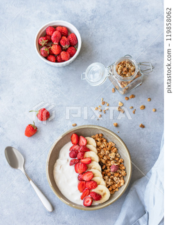 Natural greek yogurt with muesli, strawberry and banana in a bowl on a blue background Natural greek yogurt with muesli, strawberry and banana in a bowl on a blue background 119858062