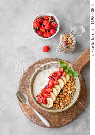 Greek yogurt with muesli, strawberry and banana in a bowl on a wooden board on a  light background  119858068