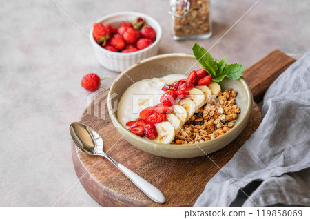 Greek yogurt with muesli, strawberry and banana in a bowl on a wooden board on a light background  119858069