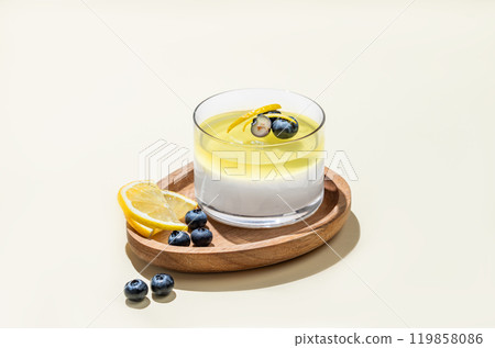 Creamy lemon panna cotta with blueberries in a glass on a wooden board on a yellow background 119858086