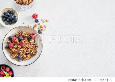 Dry muesli or granola, raspberries and blueberries in a bowl on a light background 119858100